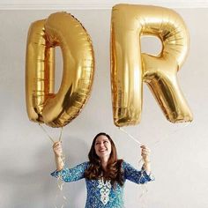 a woman holding two large gold balloons in the shape of the letter p is for po