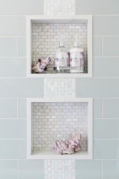 two white shelves with bottles and soaps on them in a tiled bathroom wall above a sink