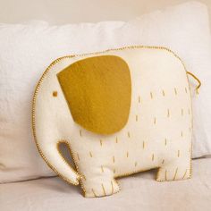 an elephant pillow sitting on top of a bed next to a white pillow with yellow trim