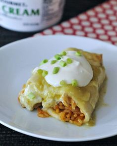 a white plate topped with an enchilada covered in cheese and sour cream