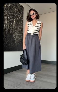 a woman standing in front of a painting holding a handbag and wearing white tennis shoes