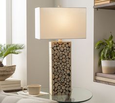 a table lamp sitting on top of a glass table next to a chair and potted plant