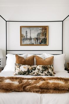 a white bed topped with pillows and blankets next to a framed painting on the wall