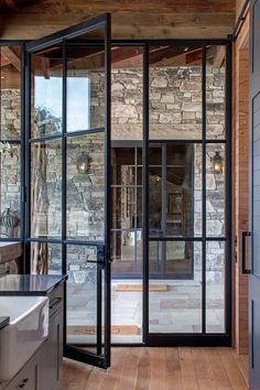 a kitchen with an open glass door leading to the outside area and stone wall behind it