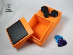 an orange box with two black knobs next to a guitar picker and some other items