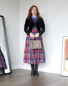 a woman standing in front of a mirror wearing a plaid dress and black jacket with fur collar