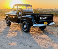 an old black pickup truck parked on the side of a dirt road at sunset or sunrise