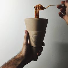 a person is holding a cup with food in it and the other hand is reaching for something