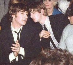 two young men sitting next to each other in front of a group of people wearing suits and ties