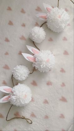 three white pom - poms with pink ears are on a polka dot sheet