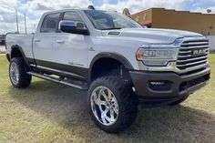 a large gray truck parked on top of a grass covered field in front of a building