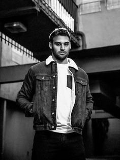 a man standing in front of a building wearing a jean jacket and white t - shirt