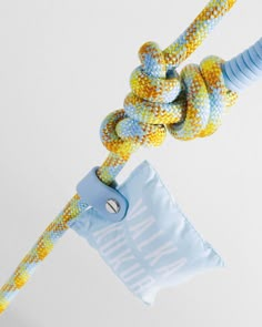 a blue and yellow rope with a pillow hanging from it's end on a white background