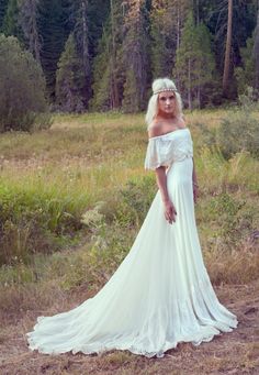 a woman wearing a white dress standing in a field with trees and grass behind her