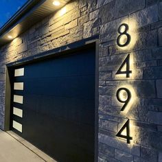 a modern house with two garage doors and numbers on the side of it at night