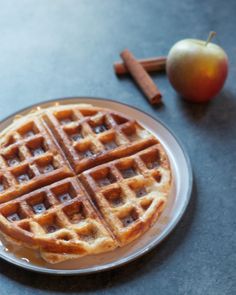 a waffle sitting on top of a plate next to an apple and cinnamon stick