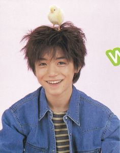 a young man with a bird on his head smiles at the camera while wearing a denim jacket and striped shirt