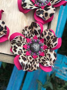 three hair clips with pink and leopard print flowers on top of a wooden table next to blue chairs