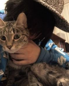 a woman holding a cat in her arms and wearing a hat on top of her head