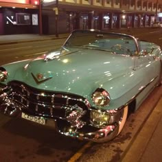 an old car parked on the side of the road in front of a building at night