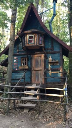 a small blue cabin in the woods with stairs leading up to it's entrance