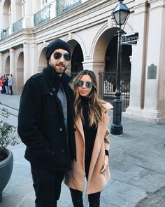 a man and woman standing next to each other in front of a building with people walking by