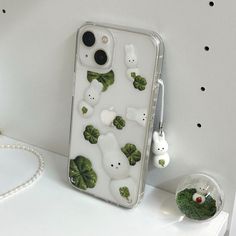 an iphone case with green leaves and white bears on it sitting on a table next to other items