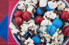 a bowl filled with red, white and blue candies next to chocolate covered popcorn