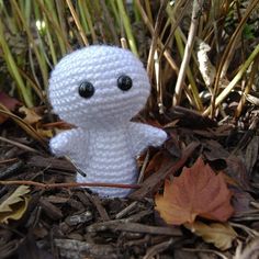 a white crocheted stuffed animal sitting in the grass next to leaves and plants