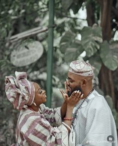 a man and woman standing next to each other talking on their cell phones in front of trees