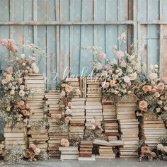 an arrangement of books and flowers are arranged in front of a blue wall with wooden planks