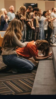 a woman kneeling down to pet a dog on the ground in front of a group of people