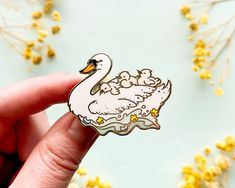 a hand holding a white swan sticker with yellow flowers in the backgroud