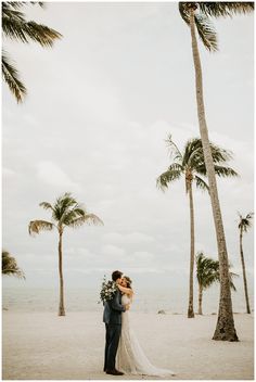 a bride and groom kissing under palm trees on the beach