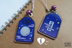 two tags are attached to a spiral notebook with purple beads and silver earwires