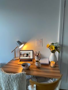 a laptop computer sitting on top of a wooden desk next to a vase with flowers