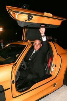 a man in a suit and tie sitting inside of a yellow sports car