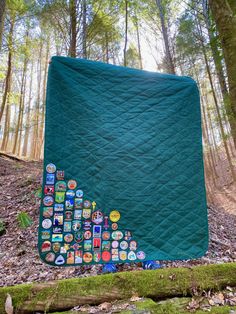 a quilted blanket with many different stickers on it sitting in the middle of a forest