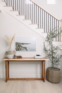 a wooden table sitting under a stair case next to a banister and potted plant