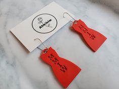 two red bow - shaped earrings are on a white piece of paper next to a sign