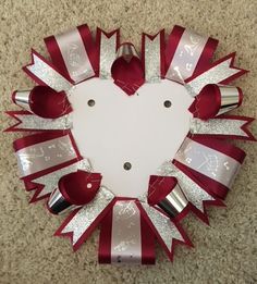 a red and white heart shaped wreath with silver ribbon around the edges on a carpeted floor