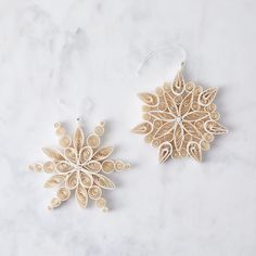 two wooden snowflakes on a white marble countertop, one is decorated with beads and the other has an ornament