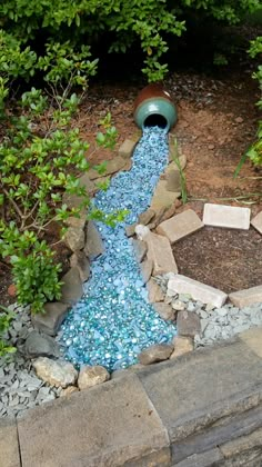 a garden with rocks, gravel and blue glass pebbles in the ground next to trees