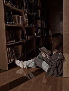 a woman sitting on the floor reading a book in front of a bookshelf