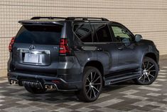 the rear end of a gray toyota land cruiser parked in front of a brick wall