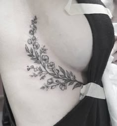 a woman's lower back tattoo with flowers and leaves on her left side ribcage