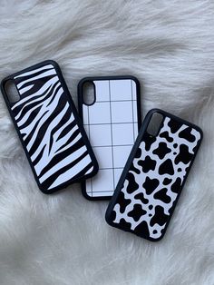 two iphone cases sitting on top of a white fur covered bed next to each other