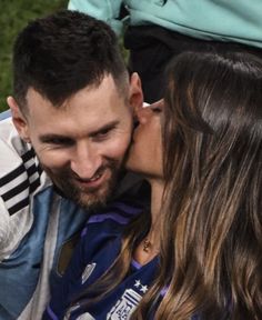 a man and woman kissing each other while sitting on a bench in front of grass