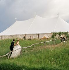 a bride and groom standing in front of a large tent