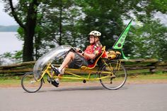 a man riding on the back of a yellow bike down a road next to a lake